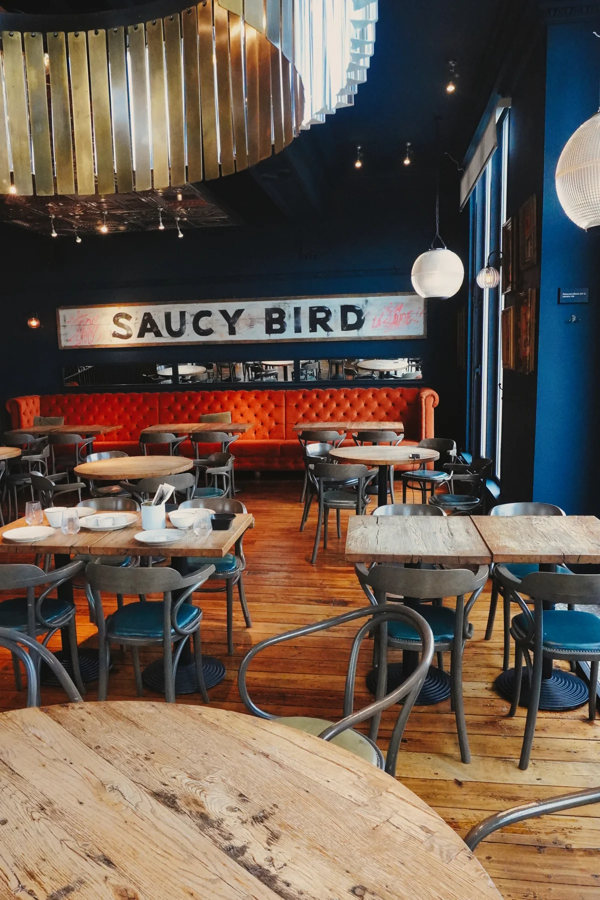 Orange banquette seating and wooden dining tables beneath the Saucy Bird sign and chandelier