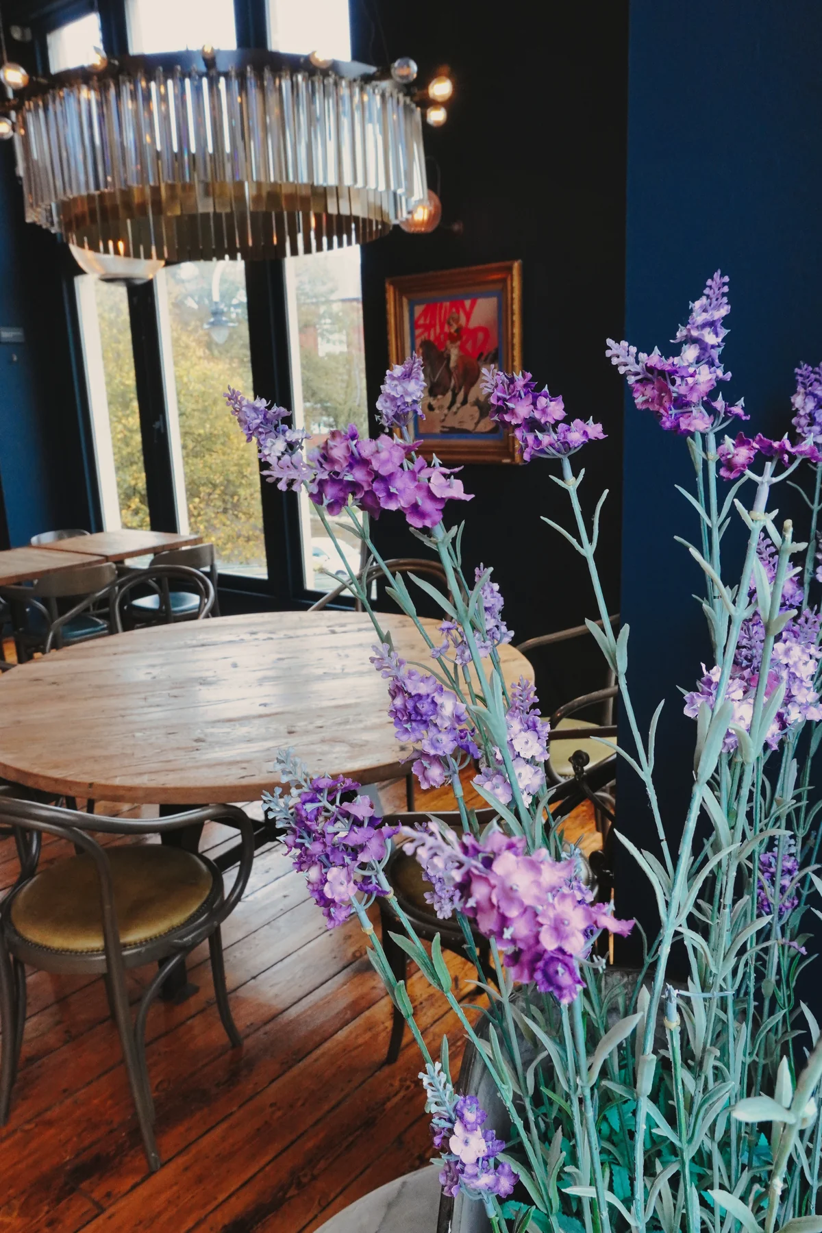 Purple flowers and set tables beneath the restaurant chandelier