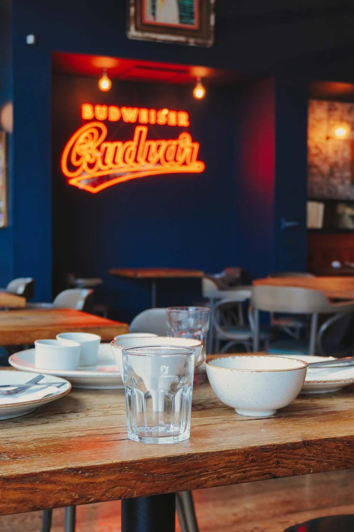 Restaurant tables and chairs below the illuminated brewery sign